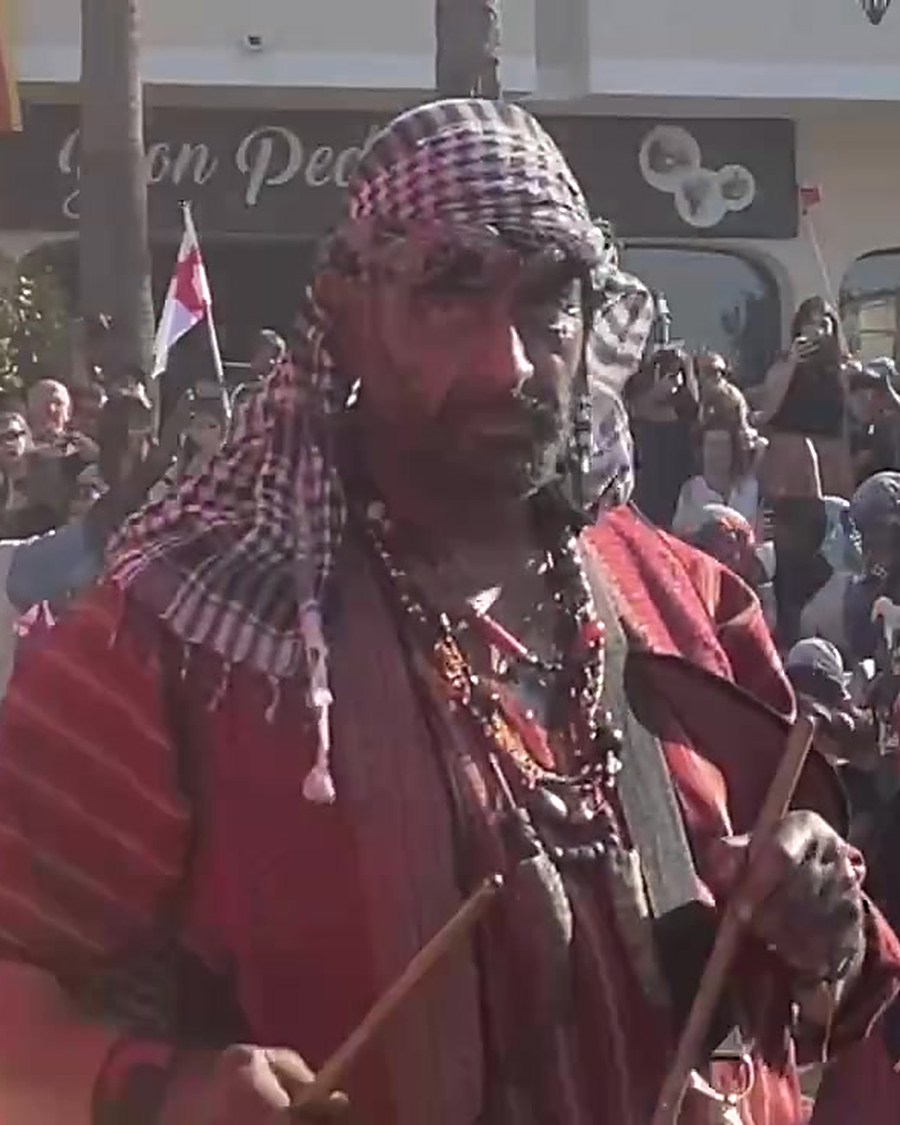 A performer in corsair costume with a sabre at Es Firó, with the red banners and the crowd behind him